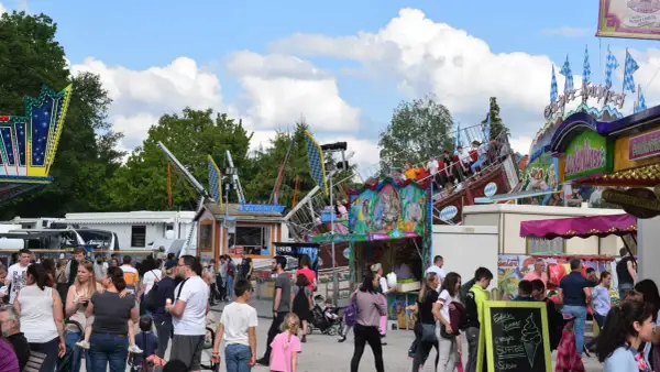 Buntes Treiben auf einem Volksfest mit Fahrgeschäften und vielen Besuchern. Ein Schiff-Karussell dreht sich, während Menschen an Ständen vorbeischlendern.