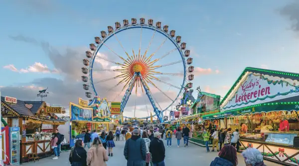 Buntes Treiben auf dem Frühlingsfest München mit Riesenrad, Essensständen und vielen Besuchern.