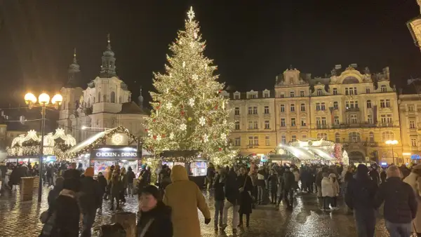 Ein festlich beleuchteter Weihnachtsbaum auf dem Prager Weihnachtsmarkt, umgeben von Buden und Menschen.